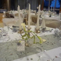 decoration de table thème couleur gris et blanc avec un chandelier garni d'arums comme centre de table, chemin de table gris brillant, nappe blanche, tout petits miroirs carrés éparpillés un peu partout sur la table et noms de tables