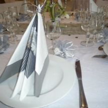 pliage de serviettes blanches grises et fleuries en forme de pyramide posées sur la table