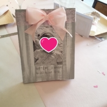 le cadre en bois a été fait main à partir d'une palette patiné de couleur gris et blanc avec un ruban de dentelle rose et un noeud en satin rose clair. Sur le cadre est collée la photo de la petite princesse avec la date du jour de son baptême.