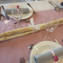 3 branches de bois flotté reliées entre elles par de la dentelle, des fleurs rose et blanches délicatement posées dessus, servant de centre de table