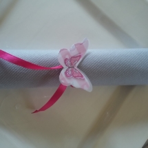 pliage de serviette de couleur gris, enroulée sur elle même, attachée par un ruban rose en satin et papillon fabriqué dans du papier scrapbooking