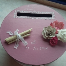 urne faite à partir d'une ancienne boite à chapeau. elle a été peinte en rose et dessus sont posées les petites décorations rappelant la déco de table à savoir bois flotté, dentelle, fleurs rose et blanche