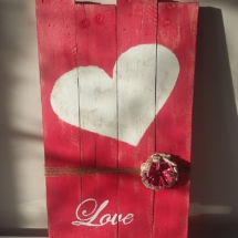 cadre en bois de palette peint en rouge avec au milieu gros coeur peint en blanc, le tout entouré de fil de jute et une fleur en tissus