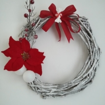 couronne de noël en branches de bois peinte en blanc et saupoudrées de fausse neige, fausse fleur de noël poinsettia rouge et gros noeud rouge posé au centre