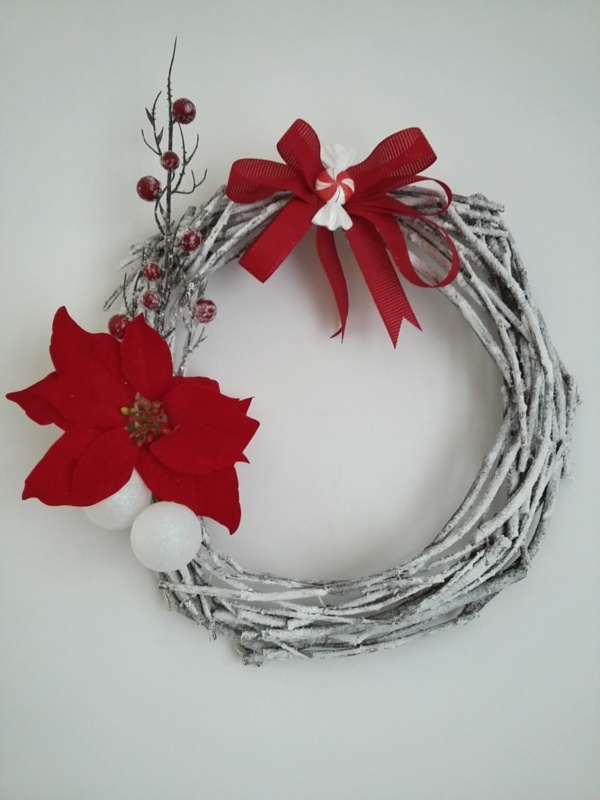 couronne de noël en branches de bois peinte en blanc et saupoudrées de fausse neige, fausse fleur de noël poinsettia rouge et gros noeud rouge posé au centre
