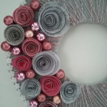 rosettes en papier de couleur gris et rose et petites boules de noël posées seulement d'un seul côté de la couronne