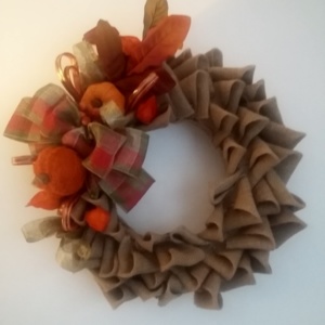 couronne de noël en toile de jute sur le thème automnale avec feuilles d'automne, petites citrouilles et gros noeud en toile de jute aux couleurs rouge et vert