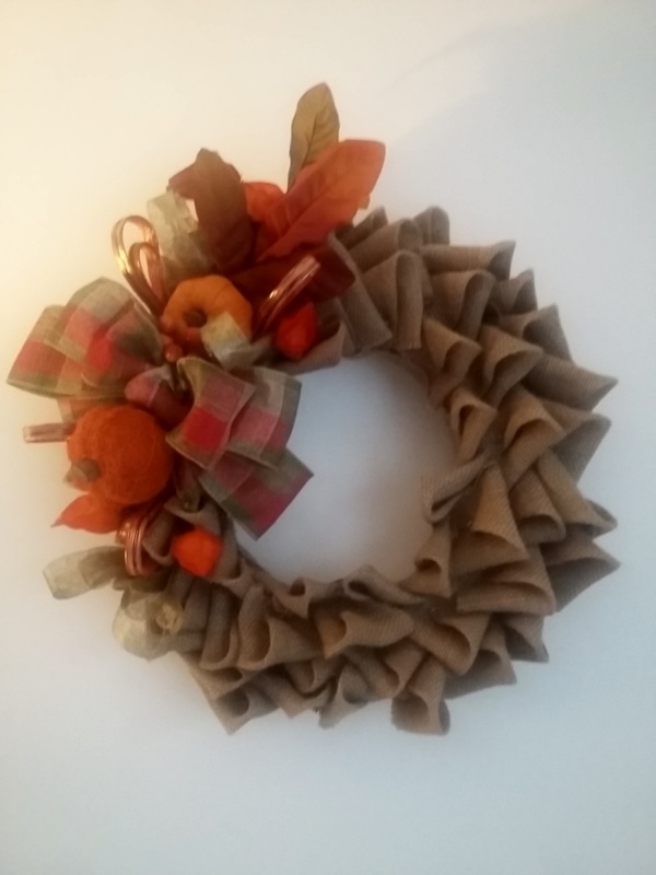 couronne de noël en toile de jute sur le thème automnale avec feuilles d'automne, petites citrouilles et gros noeud en toile de jute aux couleurs rouge et vert