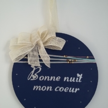 décor de porte en bois rond peint en couleur bleue nuit avec inscription blanche, gros noeud en toile de jute blanche, le tout tenu par la même toile de jute blanche. Autour du décor est inscrustée une guirlande à led pour l'éclairer la nuit.