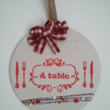 décor de porte en bois rond peint de couleur crème, gros noeud rouge et blanc, inscriptions rouge, le tout tenu par un ruban en toile de jute