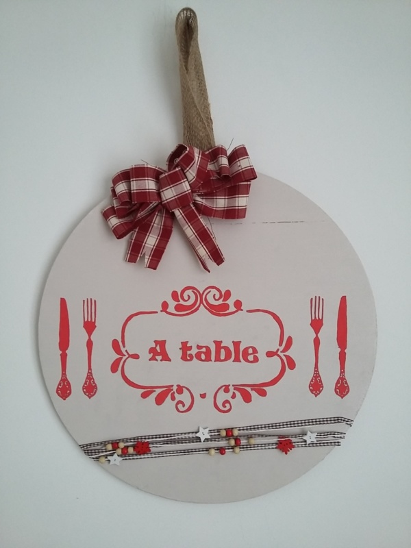 décor de porte en bois rond peint de couleur crème, gros noeud rouge et blanc, inscriptions rouge, le tout tenu par un ruban en toile de jute