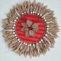 grande couronne de noël en toile de jute en forme de soleil avec au milieu de la toile de jute couleur rouge, une fleur en toile de jute naturel et fils torsadés rouge pailletés. La couronne fait 80 cm de diamètre