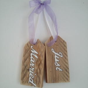 plaque de porte en bois brut avec inscriptions just married, le tout tenu par un ruban de satin blanc et un gros noeud en ruban de satin mauve transparent