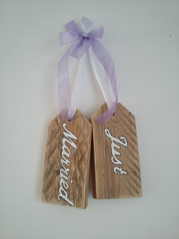 plaque de porte en bois brut avec inscriptions just married, le tout tenu par un ruban de satin blanc et un gros noeud en ruban de satin mauve transparent