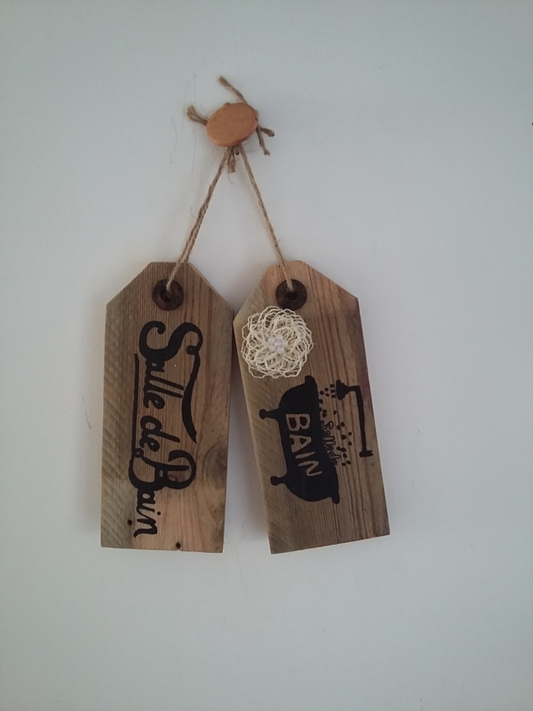 plaque de porte en bois brut avec inscriptions salle de bain et un dessin d'une baignoire peint en noire, le tout tenu par une cordelette