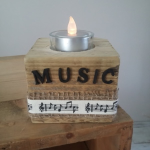 porte bougie en bois brut entouré d'un ruban en toile de jute, d'un autre ruban crème et notes de musique et sur le haut le mot music en lettres en bois noires