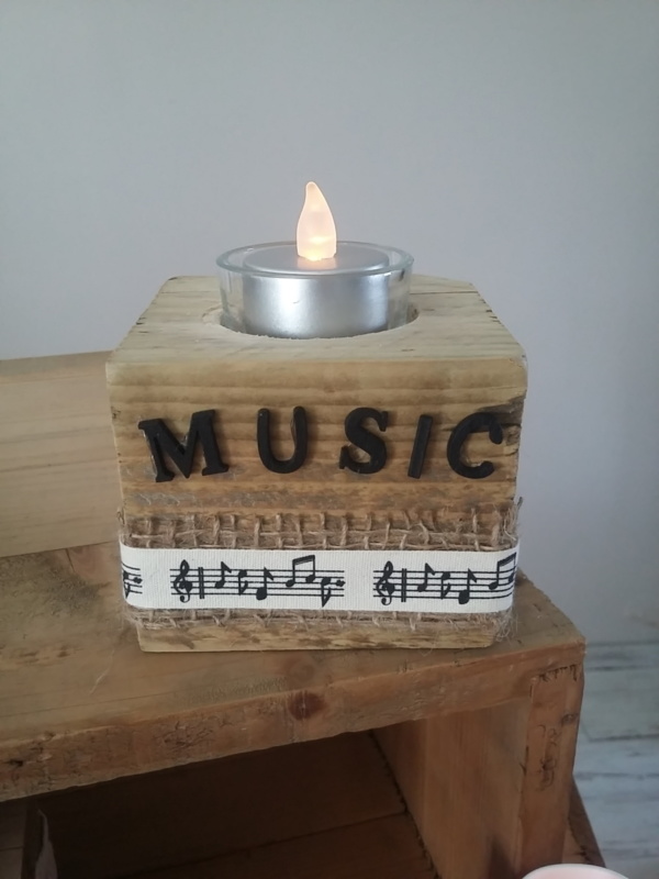 porte bougie en bois brut entouré d'un ruban en toile de jute, d'un autre ruban crème et notes de musique et sur le haut le mot music en lettres en bois noires