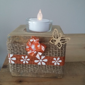 porte bougie en bois entouré d'un ruban en toile de jute et d'un ruban vintage orangé, d'une petite fleur fait main dans le même ruban vintage et sur le côté est collé un petit papillon en bois