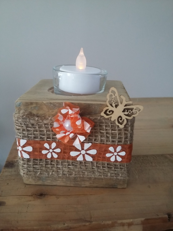 porte bougie en bois entouré d'un ruban en toile de jute et d'un ruban vintage orangé, d'une petite fleur fait main dans le même ruban vintage et sur le côté est collé un petit papillon en bois