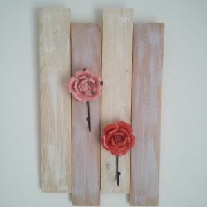 porte serviettes en bois patiné rose et blanc avec patères en porcelaine en forme de fleurs couleur rouge et rose.