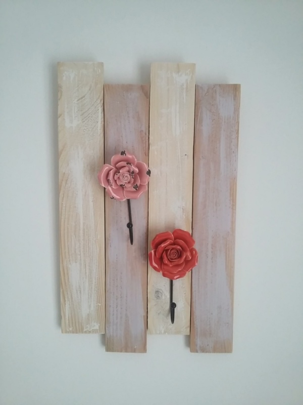 porte serviettes en bois patiné rose et blanc avec patères en porcelaine en forme de fleurs couleur rouge et rose.