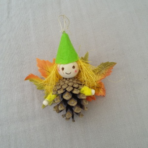 petit lutin ailé à suspendre fabriqué avec des pommes de pin, une perle de bois pour la tête, des feuilles de couleur orange jaune et vert pour les ailes et un petit chapeau pointu de couleur vert