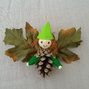 petit lutin ailé à suspendre fabriqué avec des pommes de pin, une perle de bois pour la tête, des feuilles de couleur vert foncé pour les ailes et un petit chapeau pointu de couleur vert clair