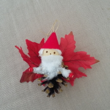 petit lutin père noël ailé à suspendre fabriqué avec des pommes de pin, une perle de bois pour la tête, des feuilles de couleur rouge pour les ailes et un petit chapeau pointu de couleur rouge.