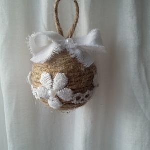 Petite boule de noël fait avec de la ficelle de lin, des bouts de dentelle blanche collés tout autour, des petits strass et un noeud en lin blanc