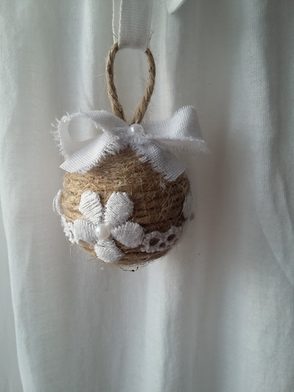 Petite boule de noël fait avec de la ficelle de lin, des bouts de dentelle blanche collés tout autour, des petits strass et un noeud en lin blanc