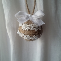 Petite boule de noël fait avec de la ficelle de lin, des bouts de dentelle blanche collés tout autour, des petits strass et un noeud en lin blanc