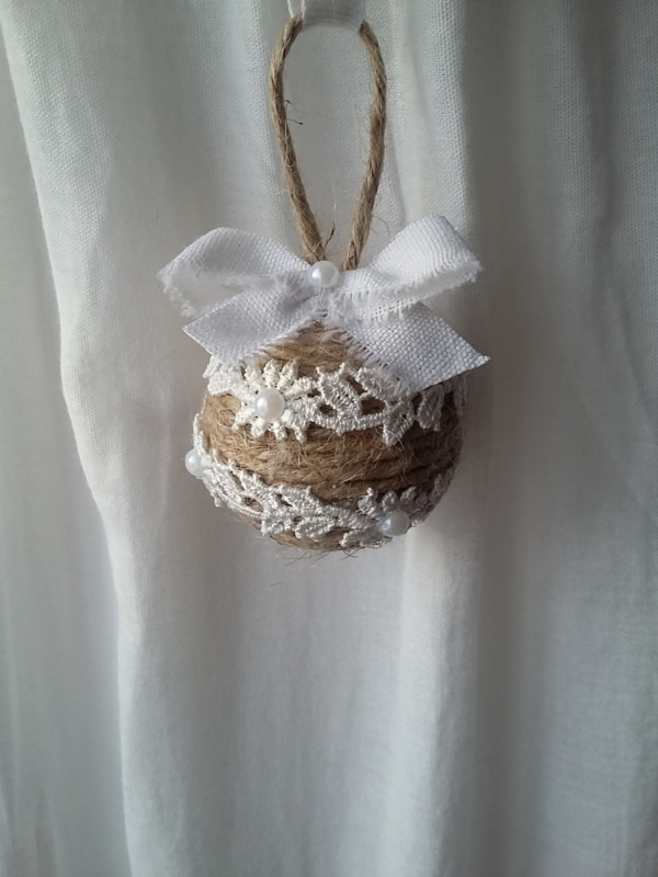 Petite boule de noël fait avec de la ficelle de lin, des bouts de dentelle blanche collés tout autour, des petits strass et un noeud en lin blanc