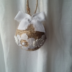 Petite boule de noël fait avec de la ficelle de lin, des bouts de dentelle blanche collés tout autour, des petits strass et un noeud en lin blanc