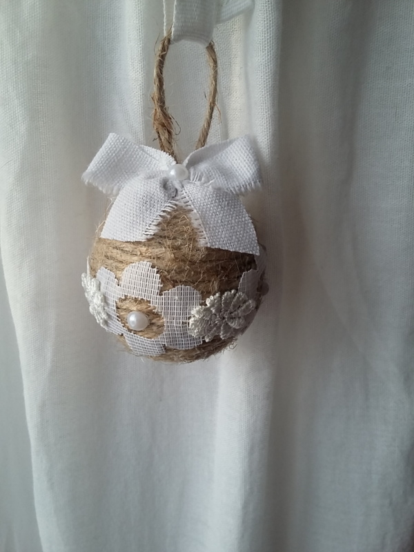 Petite boule de noël fait avec de la ficelle de lin, des bouts de dentelle blanche collés tout autour, des petits strass et un noeud en lin blanc