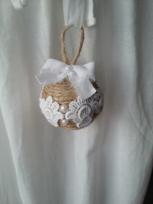 Petite boule de noël fait avec de la ficelle de lin, des bouts de dentelle blanche collés tout autour, des petits strass et un noeud en lin blanc