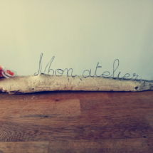 Les mots mon atelier écrit en fil de fer posé sur du bois flotté