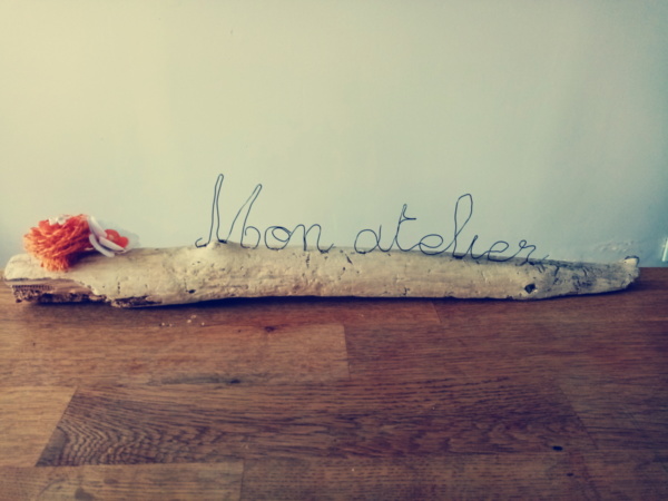 Les mots mon atelier écrit en fil de fer posé sur du bois flotté