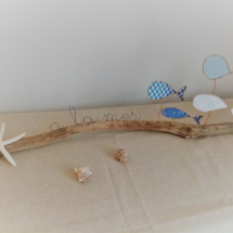 Décoration sur le thème de mer avec poissons en fil de kraft arme couleur bleue posés délicatement sur une branche de bois flotté. Une étoile de mer est collée à l'extrémité du bois.
