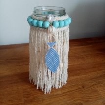 Petit bougeoir en macramé avec autour des petites perles de bois bleu ciel, une cordelette et un petit poisson bleu à petits pois blanc.