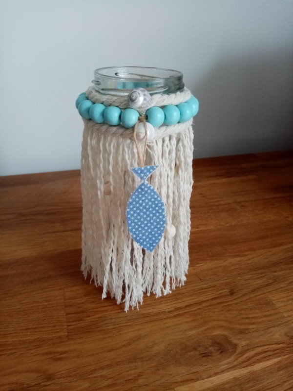 Petit bougeoir en macramé avec autour des petites perles de bois bleu ciel, une cordelette et un petit poisson bleu à petits pois blanc.