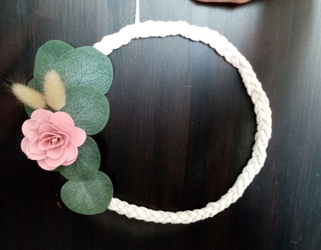 Couronne de macramé tressé avec fleur en bois de couleur rose et des petites feuilles d'eucalyptus.