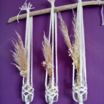 Trois soliflores en macramé suspendus sur une branche de bois flotté. Des fleurs de pampa et du gypsophile séché agrémentent ces soliflores