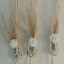 Trois soliflores en macramé suspendus sur une branche de bois flotté. Des fleurs de pampa et une petite fleur blanche en tissus agrémentent ces soliflores