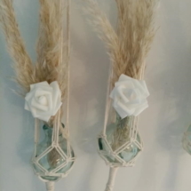 Trois soliflores en macramé suspendus sur une branche de bois flotté. Des fleurs de pampa et une petite fleur blanche en tissus agrémentent ces soliflores