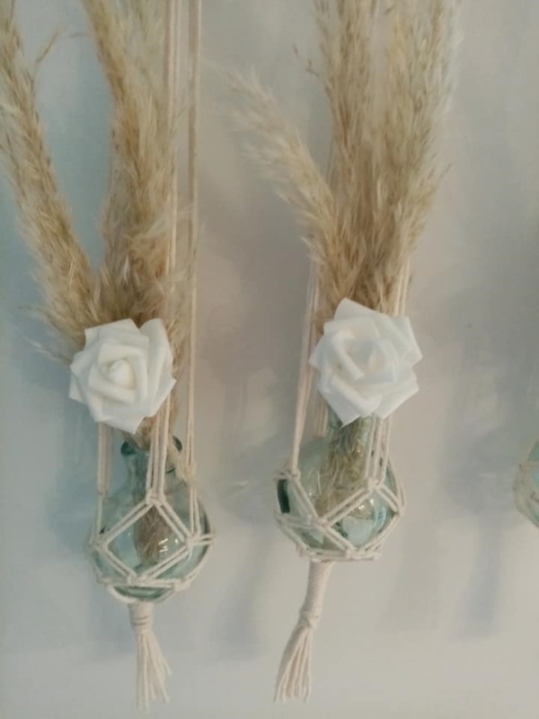 Trois soliflores en macramé suspendus sur une branche de bois flotté. Des fleurs de pampa et une petite fleur blanche en tissus agrémentent ces soliflores