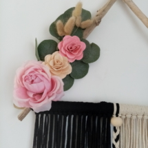 Suspension en macramé noir et blanc tenu par des branches de bois flotté placés en triangle, agrémentée de fleurs en bois, en tissus et d'eucalyptus.