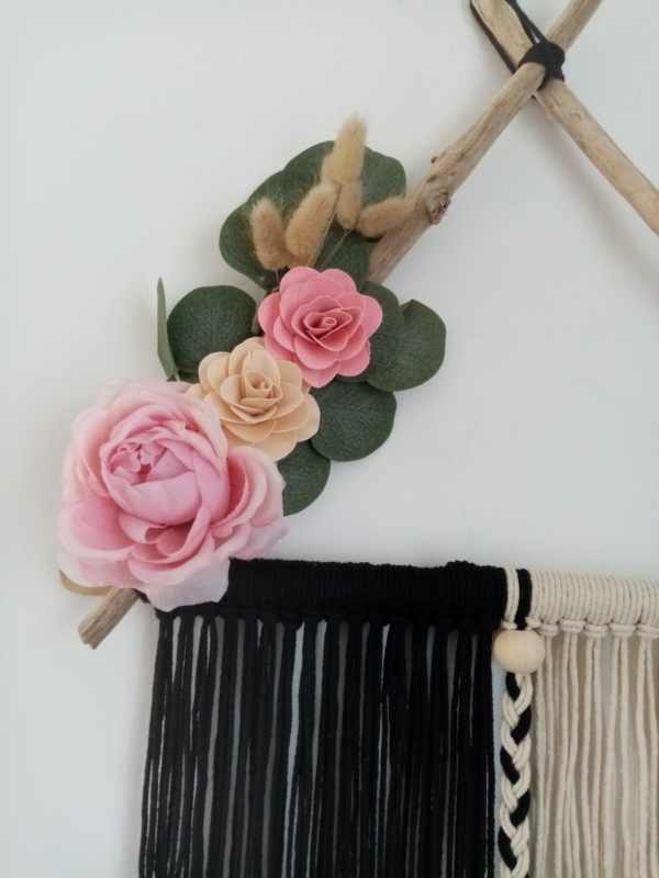 Suspension en macramé noir et blanc tenu par des branches de bois flotté placés en triangle, agrémentée de fleurs en bois, en tissus et d'eucalyptus.