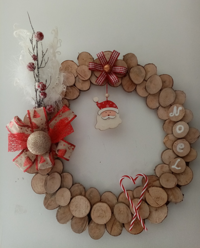 Couronne de noël avec petits rondins de bois, plume blanche, branche de houx, gros noeud et père noël en bois.