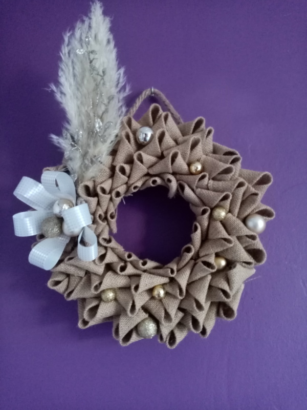 Couronne de noël en toile de jute avec fleur de pampa, branche pailletée, gros noeud et petites boules couleur or.