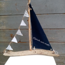Bateau en bois flotté avec une voile bleu marine et une inscription berck sur mer en broderie fait main ainsi qu'une guirlande de petits fanions tissus blanc et petits pois bleus